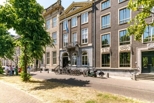Zonnige straat aan de Lange Vijverberg in Den Haag met historische gebouwen, fietsen en een groepje mensen onder de bomen.